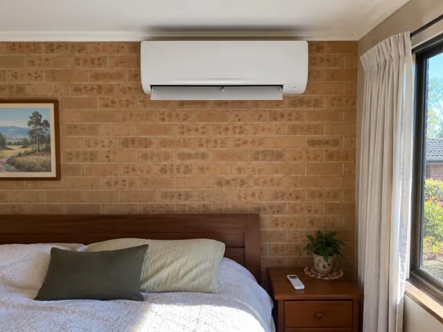 Split system indoor head above a bed on a brick bedroom wall in Happy Valley