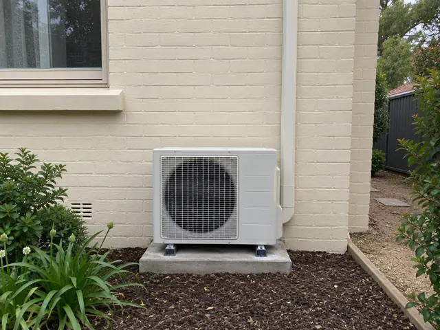 Outdoor air conditioner unit on a concrete pad beside a cream brick house in Belair